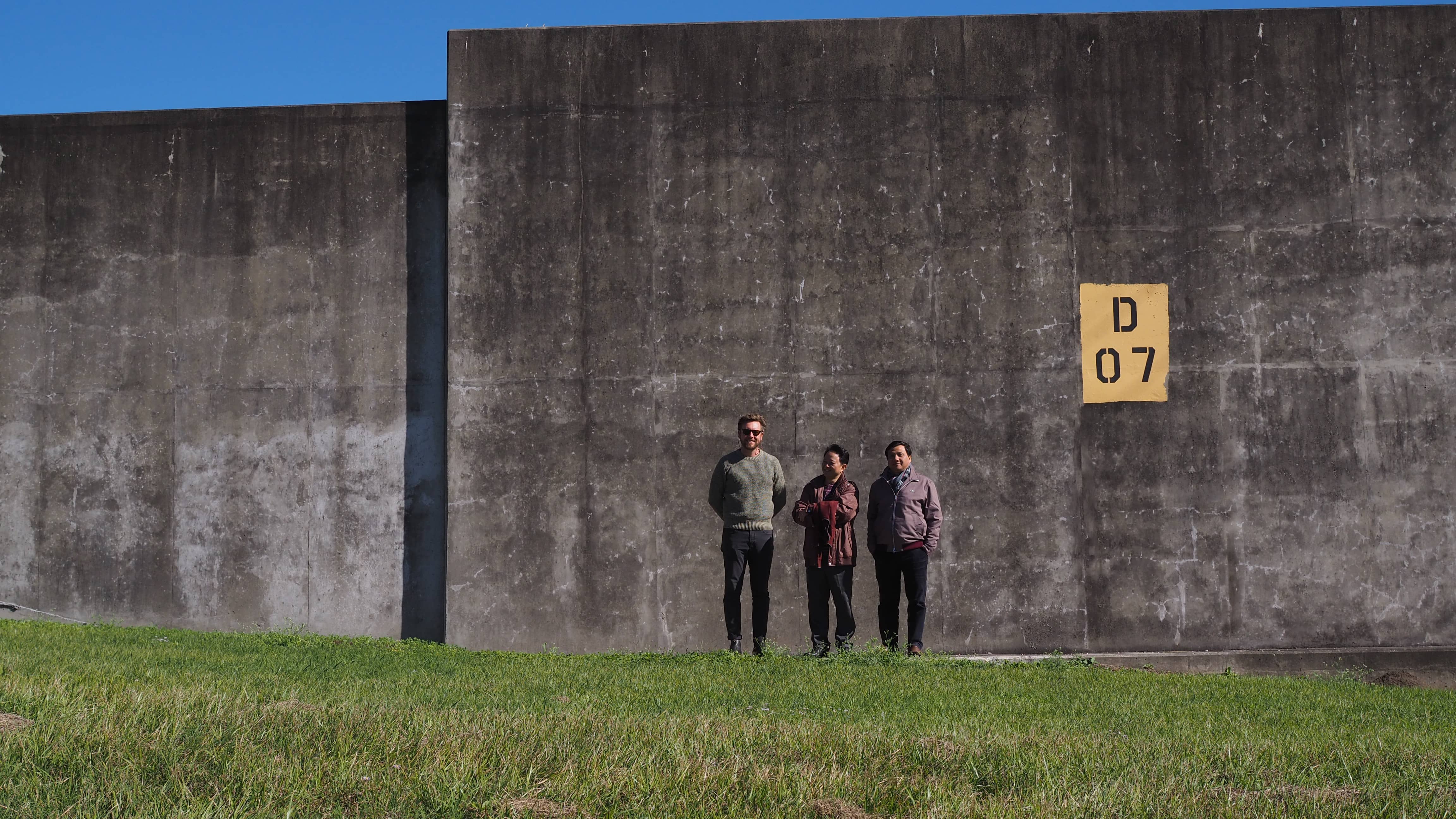 Three people standing in front of large concrete flood wall