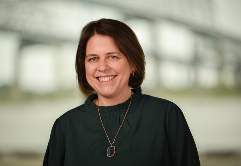 Professional portrait of a smiling woman with dark hair in a green top.
