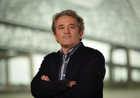 Man with graying hair, blue striped shirt and navy cardigan, arms crossed.