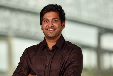 Smiling man in a dark shirt with crossed arms, blurred background.