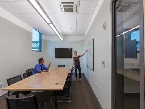 Conference room with two people, one at a whiteboard and one sitting at the table