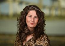 Photograph: Woman with long, curly brown hair and blue eyes, in a leopard print jacket.