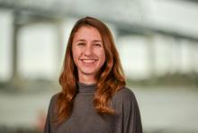 Smiling young woman with long auburn hair in a gray top.