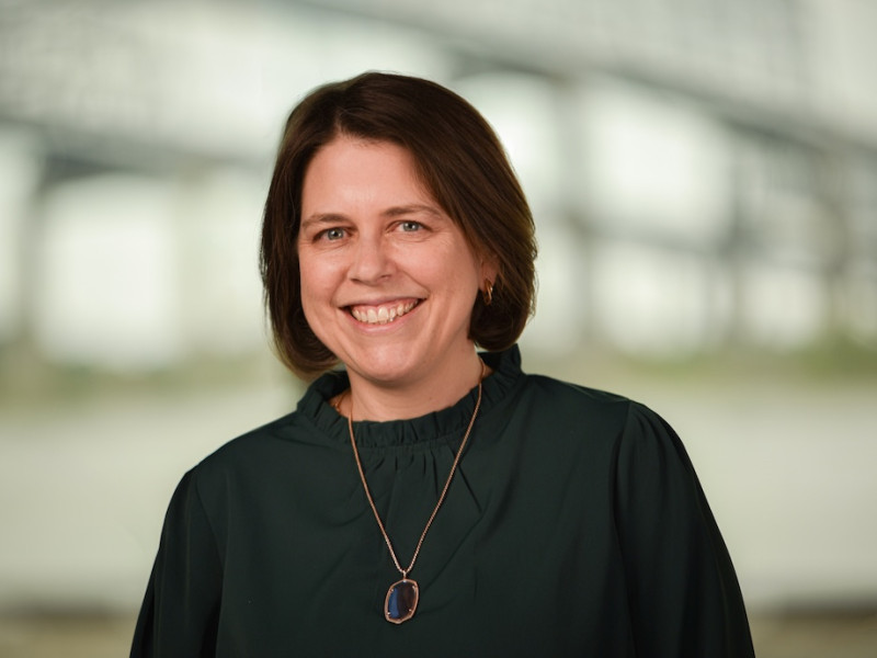 Professional portrait of a smiling woman with dark hair in a green top.