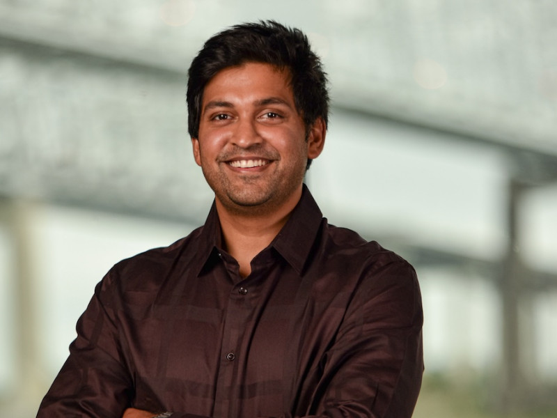 Smiling man in a dark shirt with crossed arms, blurred background.
