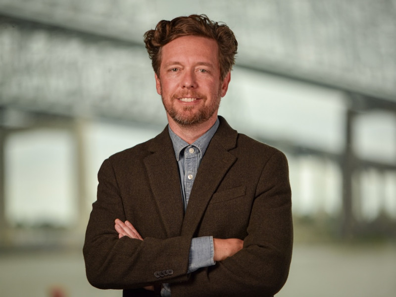 Smiling man with reddish hair and beard, wearing a brown blazer and blue shirt.